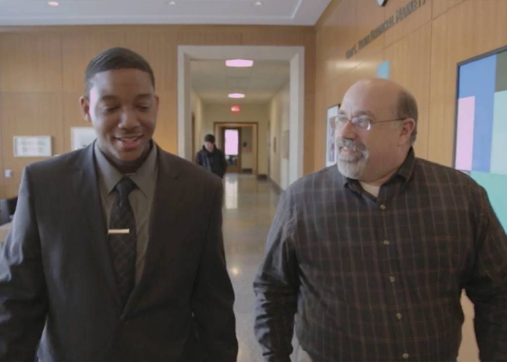 Two men, one younger, one middle-aged, having a discussion as they walk through the halls at Seidman.